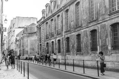 People walking on road along buildings in city