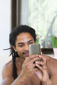Smiling shirtless man using mobile phone at home