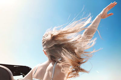 Rear view of woman with hand raised against sky