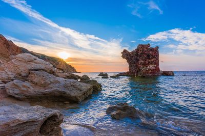 Rock formations in sea against sky during sunset