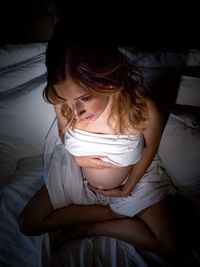 High angle view of pregnant woman sitting on bed at home