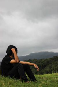 Man sitting on field against sky