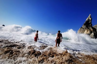 Rear view of men sitting on shore against clear sky