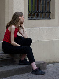 Side view of young woman sitting against wall