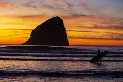 Silhouette rock in sea against sky during sunset