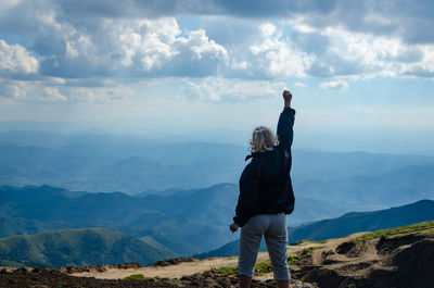 Rear view of man standing on mountain against sky