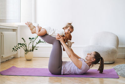 Young woman fit mom with baby girl in her legs doing fitness on mat at home