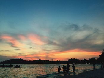 Silhouette people standing on beach against sky during sunset