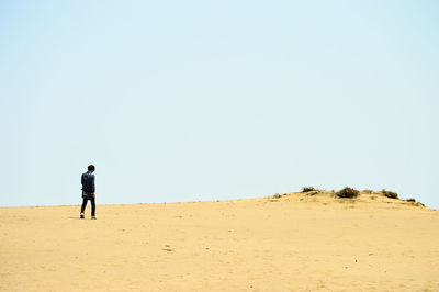 Man walking on sand dune in desert against clear sky