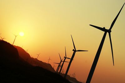 Low angle view of silhouette wind turbines against sky during sunset