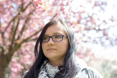 Close-up of thoughtful woman looking away while standing against flowering tree