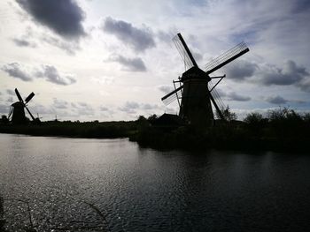 Traditional windmill by river against sky