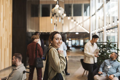 Side view portrait of smiling female entrepreneur standing in lobby at convention center