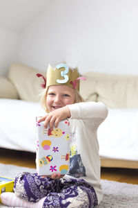 Portrait of happy girl wearing crown while holding birthday present at home