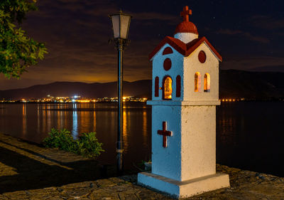 Illuminated building by lake against sky at night