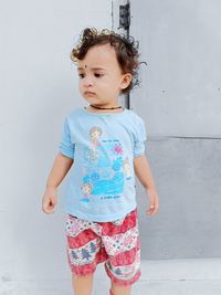 Cute girl looking away while standing against wall