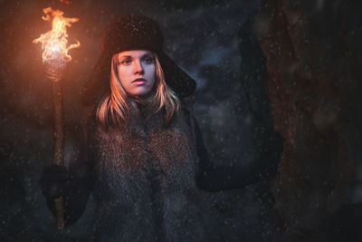 Woman with flaming torch in cave at night during winter