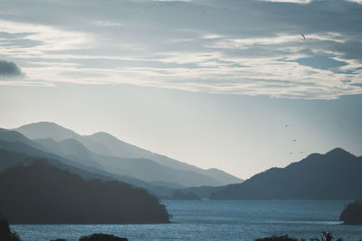 Scenic blueish view of sea by mountains against sky