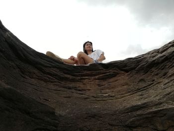 Portrait of young man sitting on rock against sky