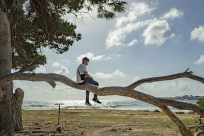 Teenager climbing a tree against the blue sky in front of the sea