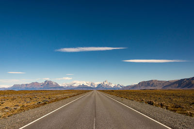 Empty road leading towards mountains against sky