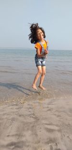 Portrait of smiling girl jumping on beach against clear sky