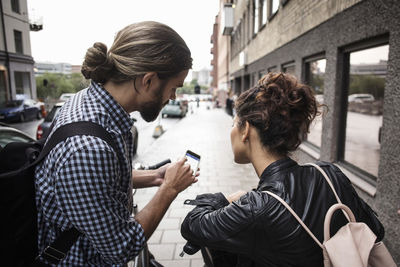 Man showing smart phone to friend on sidewalk in city