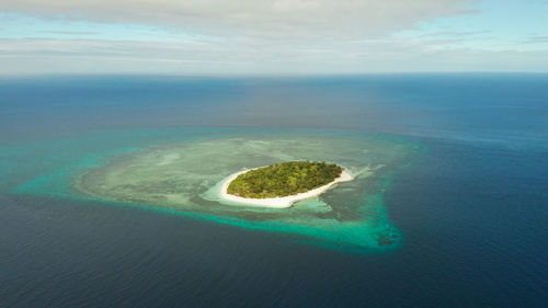 Tropical island mantigue and sandy beach surrounded by atoll coral reef and blue sea, aerial view. 