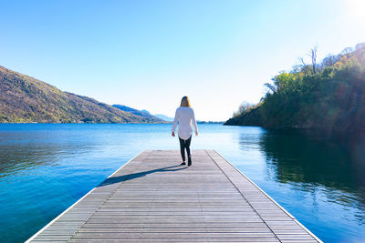 Rear view of woman walking on pier against lake