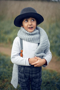 Boy child in plaid pants, hat, suspenders and scarf stands in a field in autumn