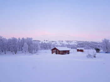 Snow covered field by houses against sky during winter