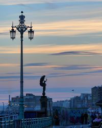 Statue of illuminated street light in city against sky