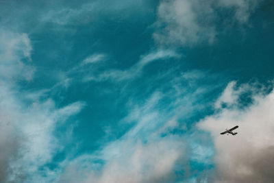 Low angle view of airplane flying in cloudy sky