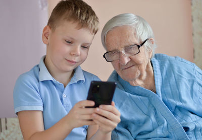 Happy elderly 90-year-old woman with glasses and her grandsone smiles using a smartphone.