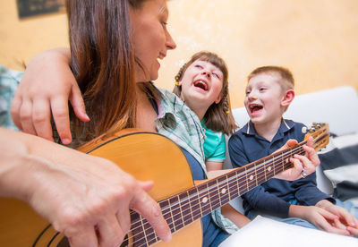 Mother playing guitar while sitting with kids at home