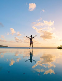 Rear view of woman standing in sea against sky during sunset