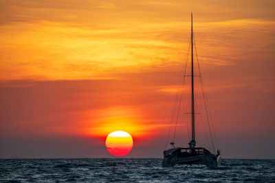 Silhouette sailboat on sea against orange sky