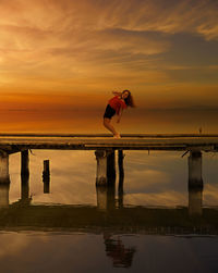 Side view of woman standing by sea against sky during sunset