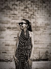 Young woman wearing sunglasses standing against brick wall