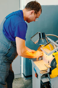 A caucasian worker in uniform sharpens a part on a machine in a workshop. manual processing of metal