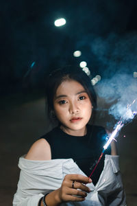 Portrait of young woman holding illuminated sparkler at night