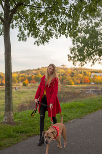 Rear view of woman with dog on road against trees