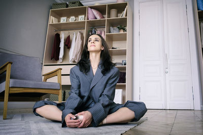 Ballerina in a gray striped suit is sitting stretching on the floor in the dressing room