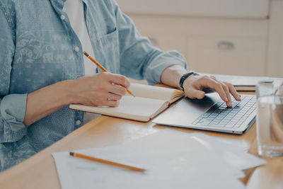 Midsection of man using laptop while sitting by table