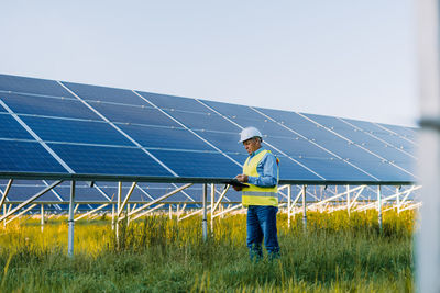 Industrial senior man engineer in uniform walking through solar panel field for examination