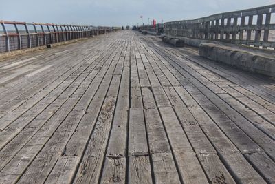 Surface level of pier on footbridge against sky