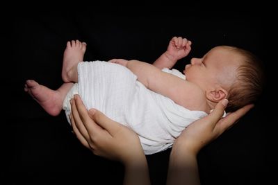 Cropped image of parent holding baby against black background