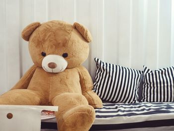 Teddy bear by cushions on bed at home