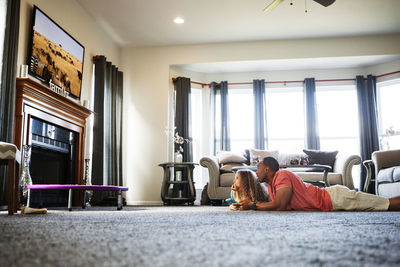 Father and daughter watching tv while lying on carpet at home