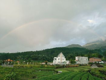 Houses on field against rainbow in sky
